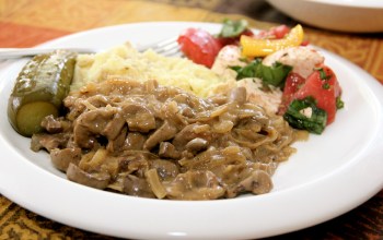 Veal Kidney Stroganoff served with mashed potatoes, pickle, and basic tomato salad