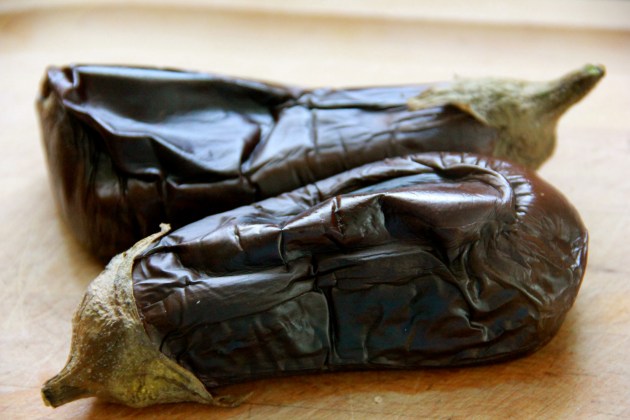 Eggplants fully roasted, resting on a board