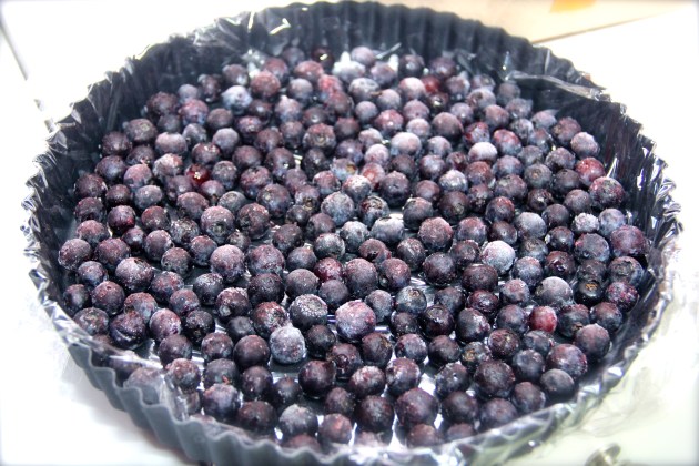 Frozen blueberries arrange on a bottom of a tart pan